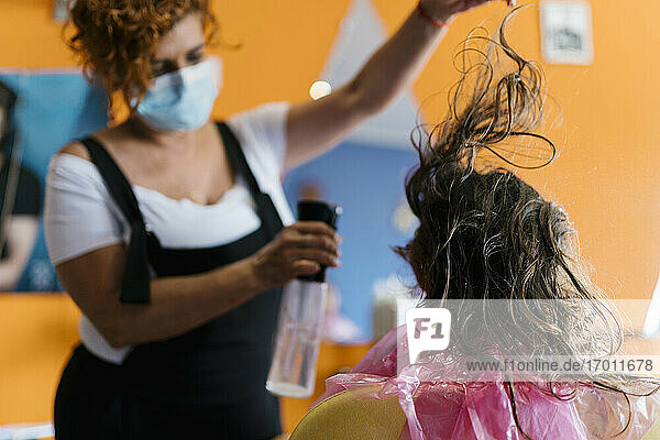 Friseurin sprüht Wasser auf das braune Haar eines Mädchens im Friseursalon
