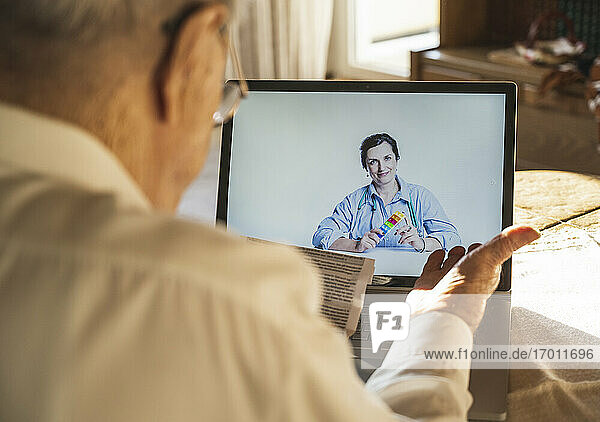 Ein männlicher Patient liest  während eine Ärztin per Videoanruf auf einem Laptop zu Hause berät