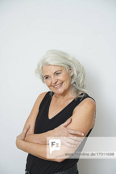 Smiling senior woman hugging herself against white background