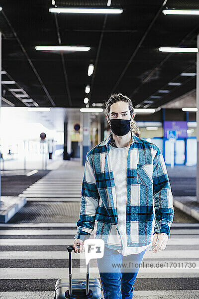 Young man wearing face mask walking with luggage on underpass road