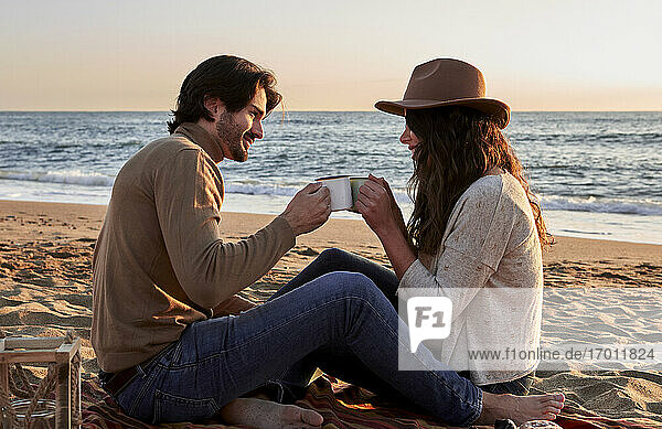 Freundin und Freund Toasting Kaffeetasse beim Sitzen am Strand