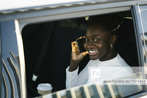 Lächelndes Teenager-Mädchen beim Telefonieren durch das Autofenster gesehen