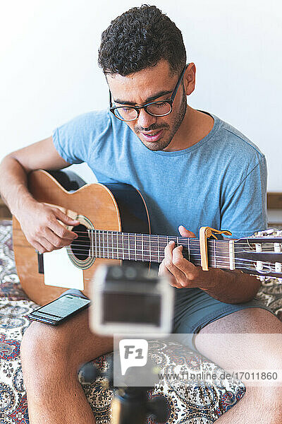 Männlicher Musiker  der Gitarre spielt  um einen Videoblog zu Hause zu erstellen