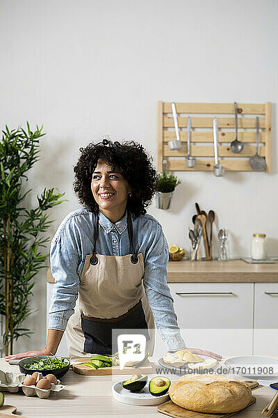 Porträt einer jungen Frau  die sich auf den Küchentisch stützt und wegschaut
