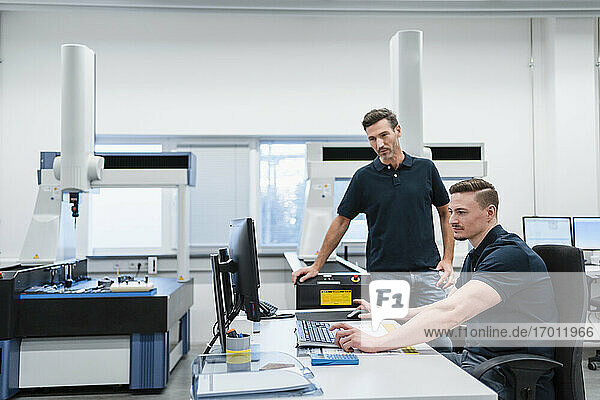 Male technician with colleague using computer in industry office