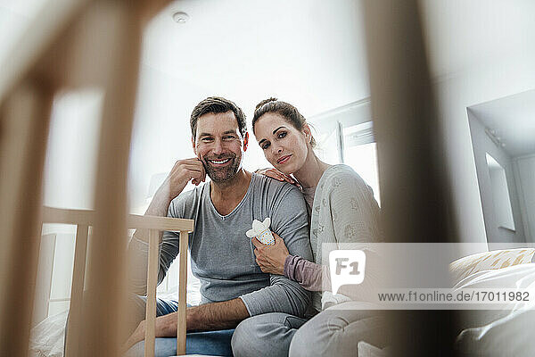 Smiling couple looking at crib in bedroom in apartment