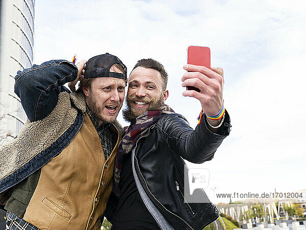 Cheerful man taking selfie with boyfriend while standing against sky