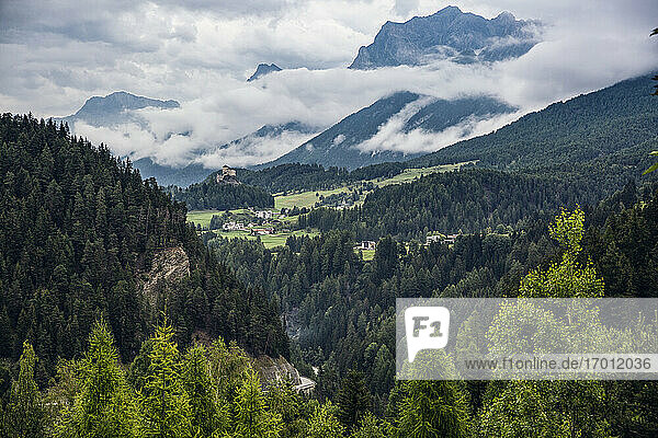 Schweiz  Kanton Graubünden  Scuol  Grünes bewaldetes Tal mit Schloss Tarasp im fernen Hintergrund