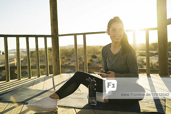 Lächelnde junge Frau  die ein Smartphone benutzt  während sie auf einer Matte im Pavillon sitzt