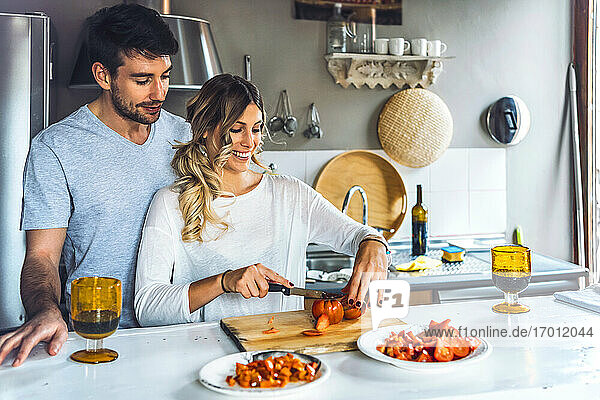 Junge Frau hackt Tomaten  während sie Abendessen kocht und ein Mann zusieht