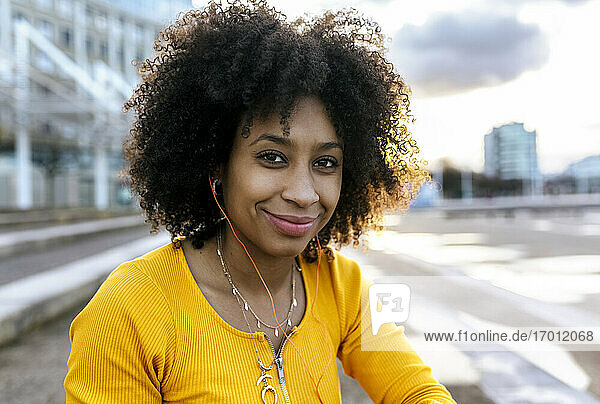 Nahaufnahme einer lächelnden Frau mit Afro-Haar  die über Kopfhörer Musik hört  gegen den Himmel