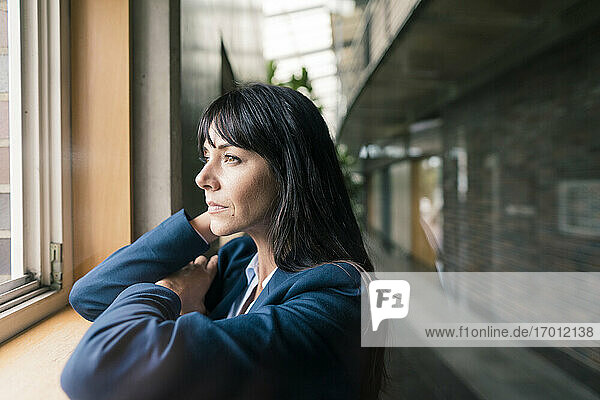 Female entrepreneur leaning while looking through window at office