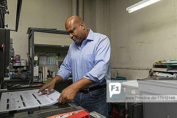 Männlicher Angestellter prüft Kopien an einer Maschine in einer Druckerei