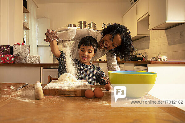 Fröhliche Mutter schreit beim Mischen von Zutaten mit ihrem Sohn auf dem Tisch in der Küche