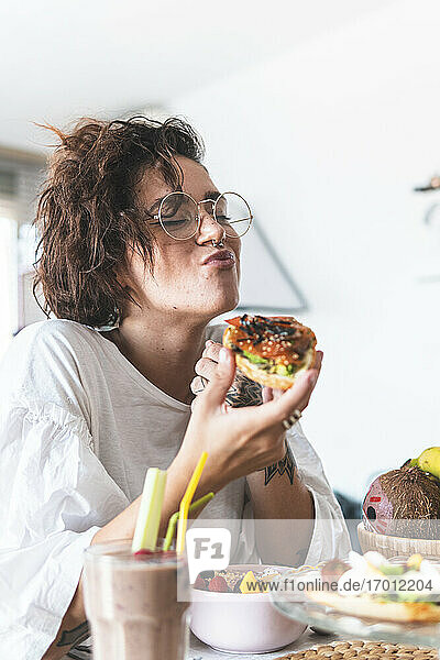 Porträt einer jungen Frau mit Brille und Nasenring beim Frühstück