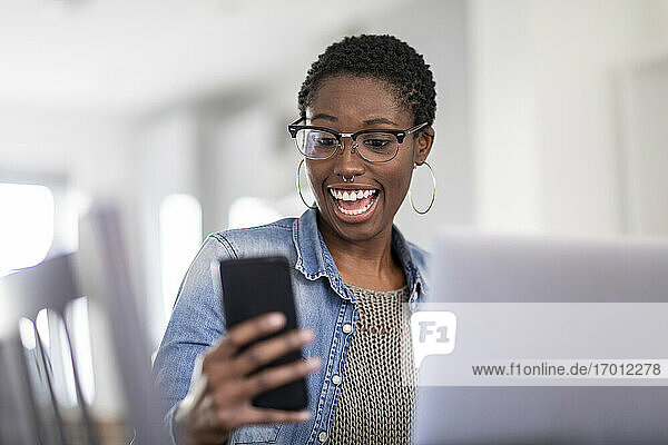 Lächelnde Frau schaut zu Hause auf ihr Smartphone