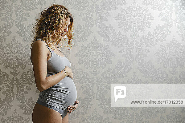 Schwangere Frau mit blondem Haar an der Wand zu Hause