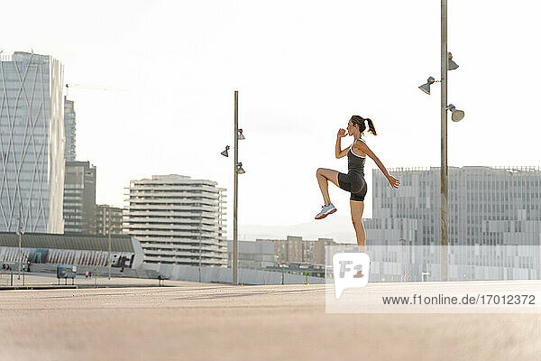 Mittlere erwachsene Sportlerin bei einer Sprungübung an einem sonnigen Tag in der Stadt