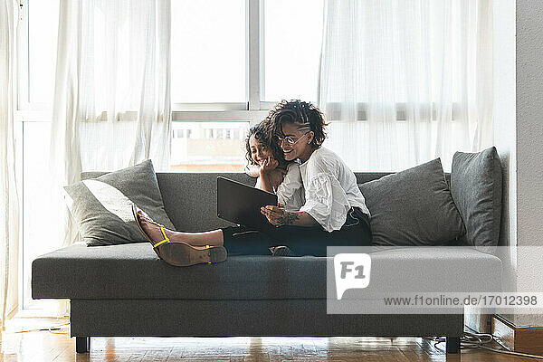 Mutter und Tochter sitzen zusammen auf dem Sofa mit digitalem Tablet