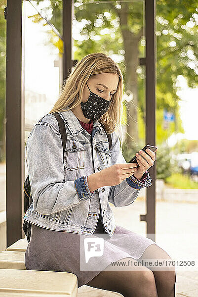 Junge Frau benutzt ihr Smartphone an der Bushaltestelle während einer Pandemie