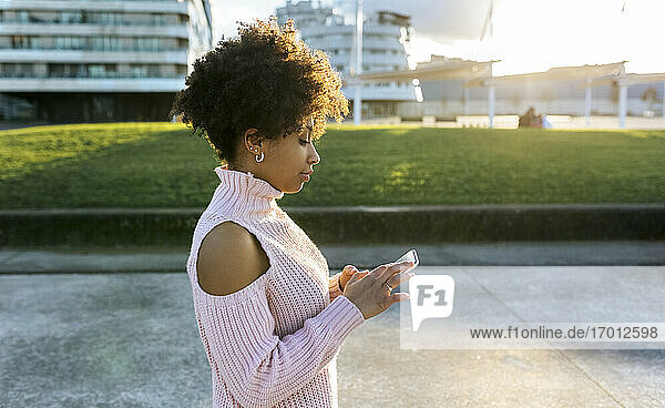 Frau mit Afro-Haar  die ein Mobiltelefon benutzt  während sie auf der Straße in der Stadt steht