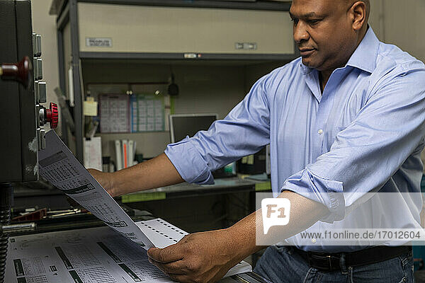 Älterer Vorgesetzter  der die Qualität des Papiers prüft  während er an der Druckmaschine im Geschäft steht