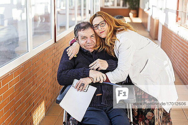 Weibliche Pflegekraft umarmt einen behinderten Mann  der in einem Pflegeheim im Rollstuhl sitzt