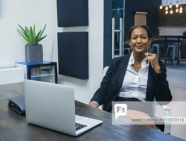 Porträt der lächelnden Geschäftsfrau sitzt am Schreibtisch im Büro