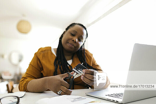 Frau schneidet Kreditkarte mit Schere bei der Arbeit im Home-Office