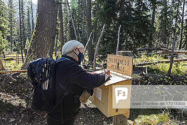 USA  Idaho  Stanley  Senior woman in protective mask signing wilderness permit before hiking