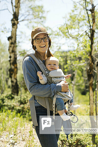 USA  Utah  Uinta National Park  Portrait of smiling woman with baby son (6-11 months) in baby carrier in forest