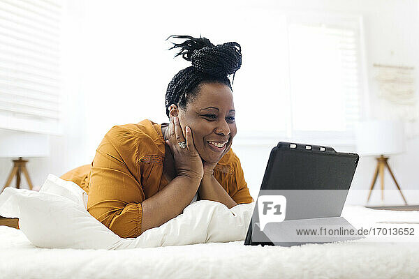 Lächelnde Frau auf dem Bett liegend und Blick auf Tablette