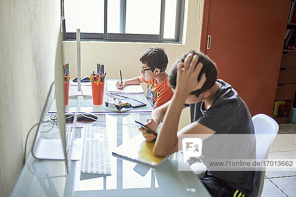 Zwei Jungen (8-9  14-15) lernen am Schreibtisch zu Hause während der Covid-19-Sperre