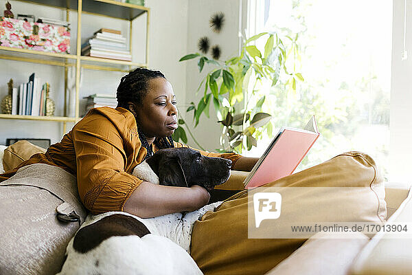 Woman reading book on sofa with her dog