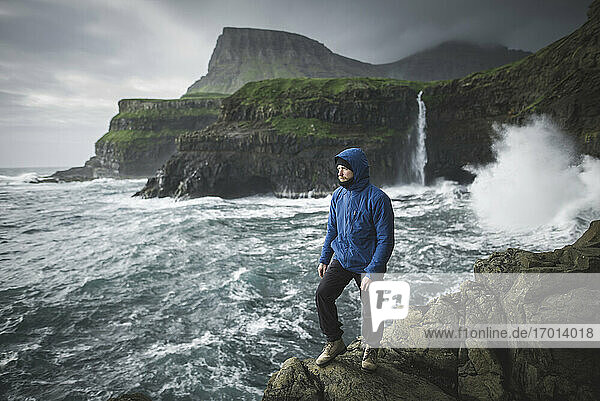 Denmark  Faroe Islands  Gasadalur village  Mulafossur Waterfall  Man standing on cliff with Mulafossur Waterfall in background