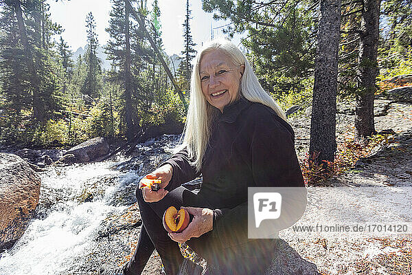 USA  Idaho  Stanley  Senior weiblichen Wanderer lächelnd und Schneiden frischen Pfirsich neben dem Bach