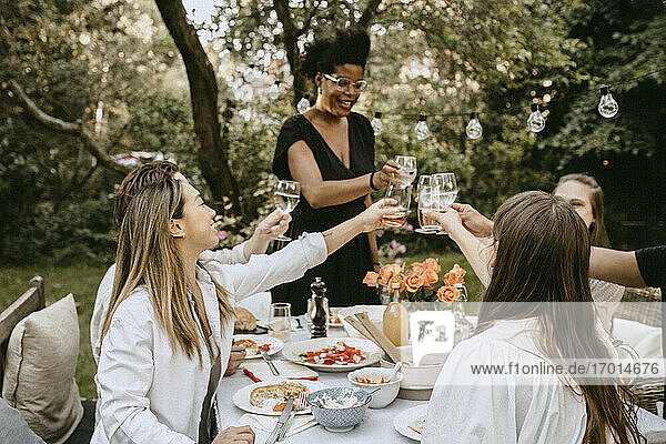Lächelnde Frau toasting Getränke mit Freunden über Tisch während geselliges Beisammensein