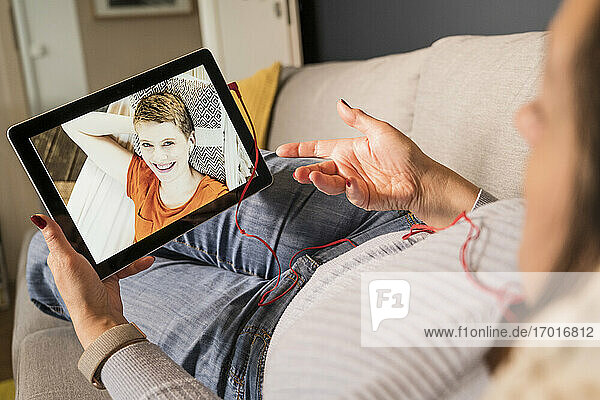 Reife Frau gestikuliert bei einem Videoanruf mit einem Freund im Wohnzimmer