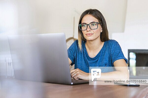 Geschäftsfrau mit Brille  die im Heimbüro auf einen Laptop schaut