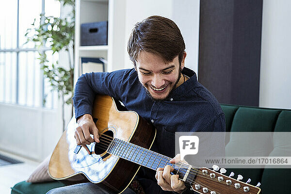 Smiling guitarist playing guitar while sitting on sofa at studio