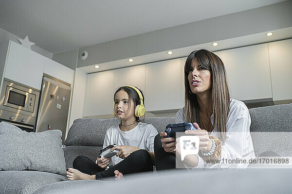 Mother and daughter playing video games together in living room