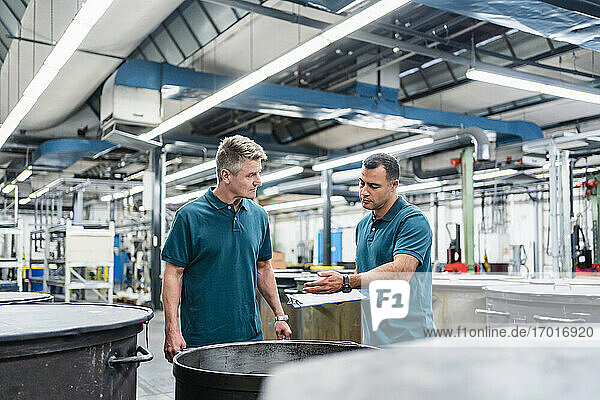 Männlicher Ingenieur im Gespräch mit einem Kollegen  während er bei einem Container in einer Fabrik steht