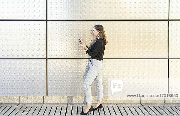 Geschäftsfrau  die ein Mobiltelefon benutzt  während sie an einer silbernen Wand steht
