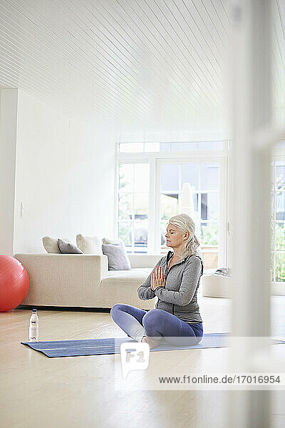 Ältere Frau mit geschlossenen Augen meditiert im Wohnzimmer