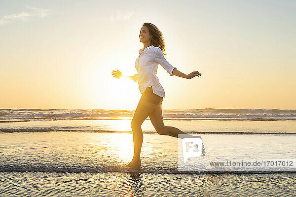 Glückliche Frau schaut weg  während sie bei Sonnenuntergang gegen das Meer läuft