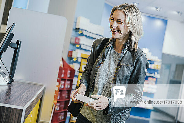 Lächelnde Kundin mit Medikamenten an der Kasse einer Apotheke
