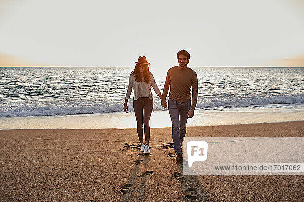 Paar hält sich beim Spazierengehen am Strand an den Händen