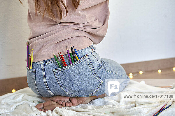 Künstlerin mit einem Bündel Buntstifte in der Gesäßtasche einer Jeans zu Hause