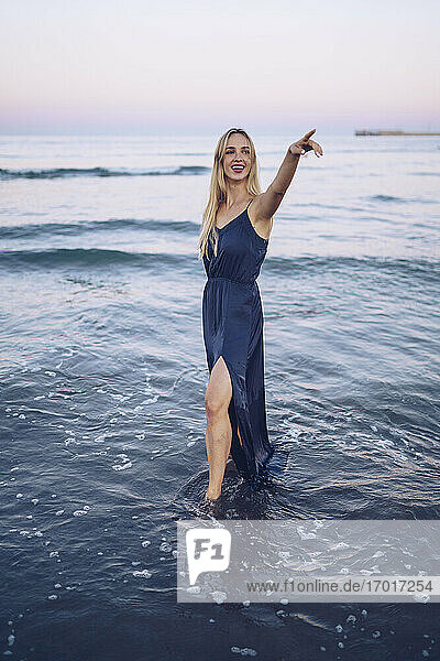 Smiling woman pointing while standing in water at Platja de Llevant beach