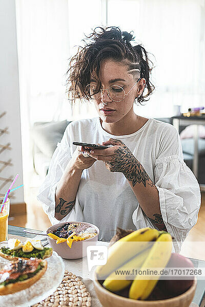 Porträt einer jungen Frau  die beim Frühstück mit ihrem Smartphone spielt